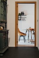 A doorway leading to a room with a wooden cabinet, a chair, a small table, and wall-mounted shelves with decorative items.