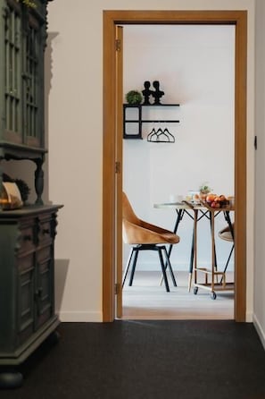 A doorway leading to a room with a wooden cabinet, a chair, a small table, and wall-mounted shelves with decorative items.