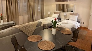 Ein modernes Hotelzimmer mit Bett, Nachttischen, einem Esstisch und einem großen Fenster mit Vorhängen.