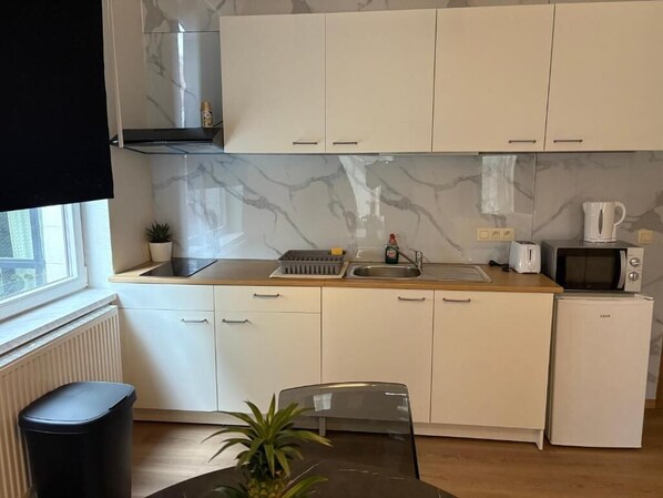 Een kleine keuken met witte kastjes, een magnetron, een spoelbak en een kleine koelkast.