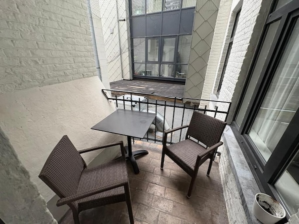 A small outdoor patio with a table and two chairs, a metal railing, and a window. - Center Monet (Ghent)