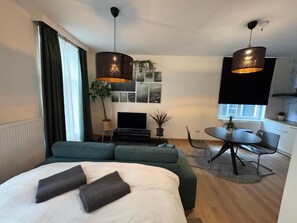 A modern hotel room with a bed, green sofa, dining table, and two pendant lights. - Center Monet (Ghent)