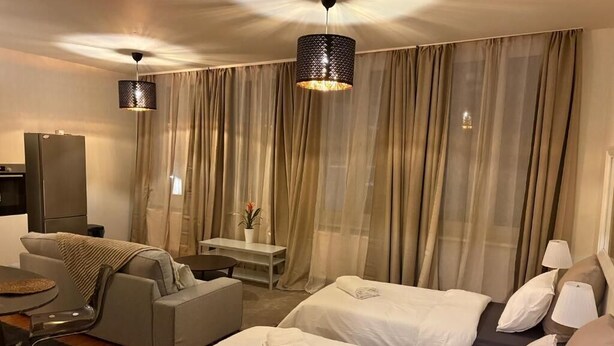 Ein Hotelzimmer mit zwei Betten, einem Schlafsofa, einem Schreibtisch, einem Stuhl, einem Fernseher und Vorhängen.