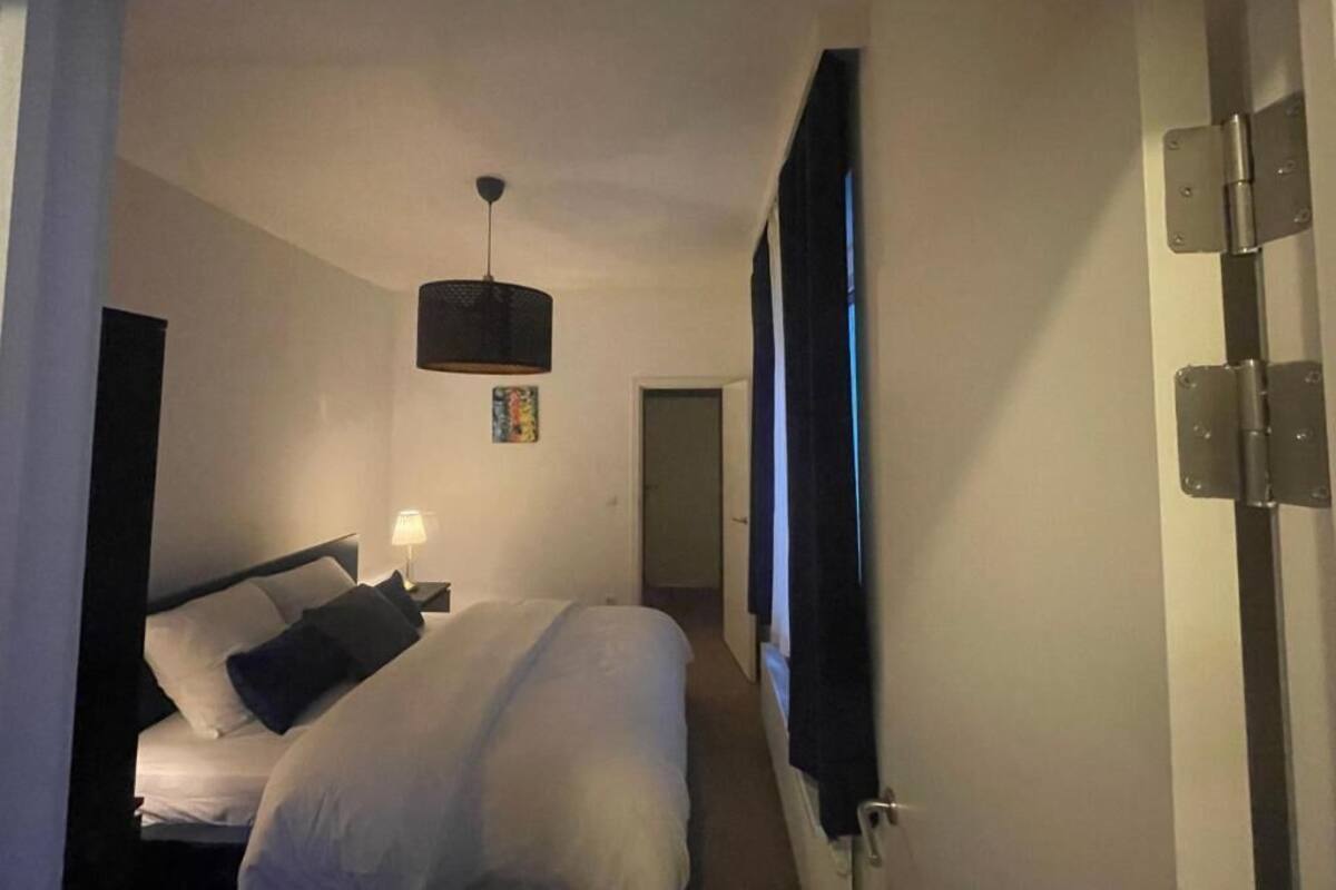 A hotel room with a bed, a hanging light fixture, a door with a mirror, and a window with curtains.