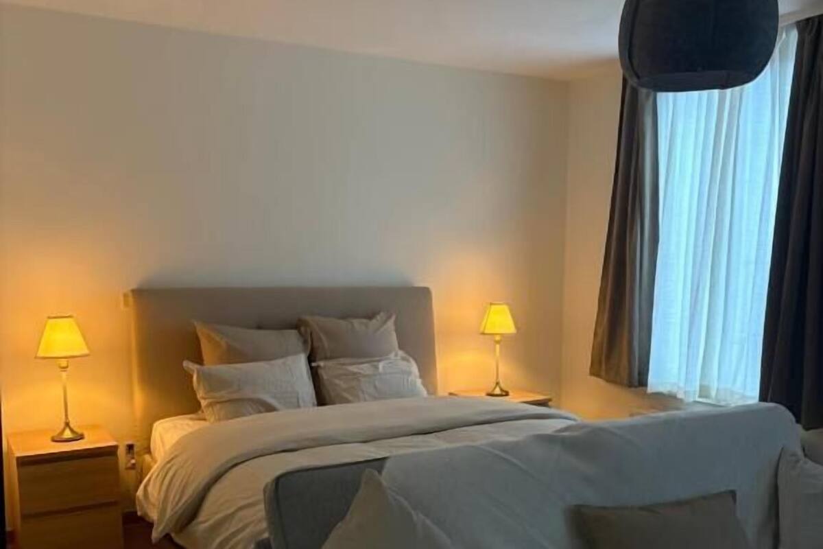 A bedroom with a bed, bedside tables, lamps, and a hanging light fixture.