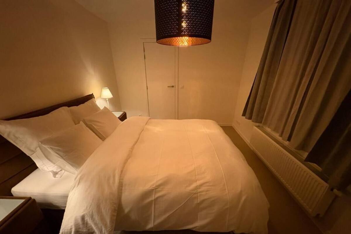 A hotel room with a bed, a nightstand, a lamp, a window with curtains, and a ceiling light fixture.