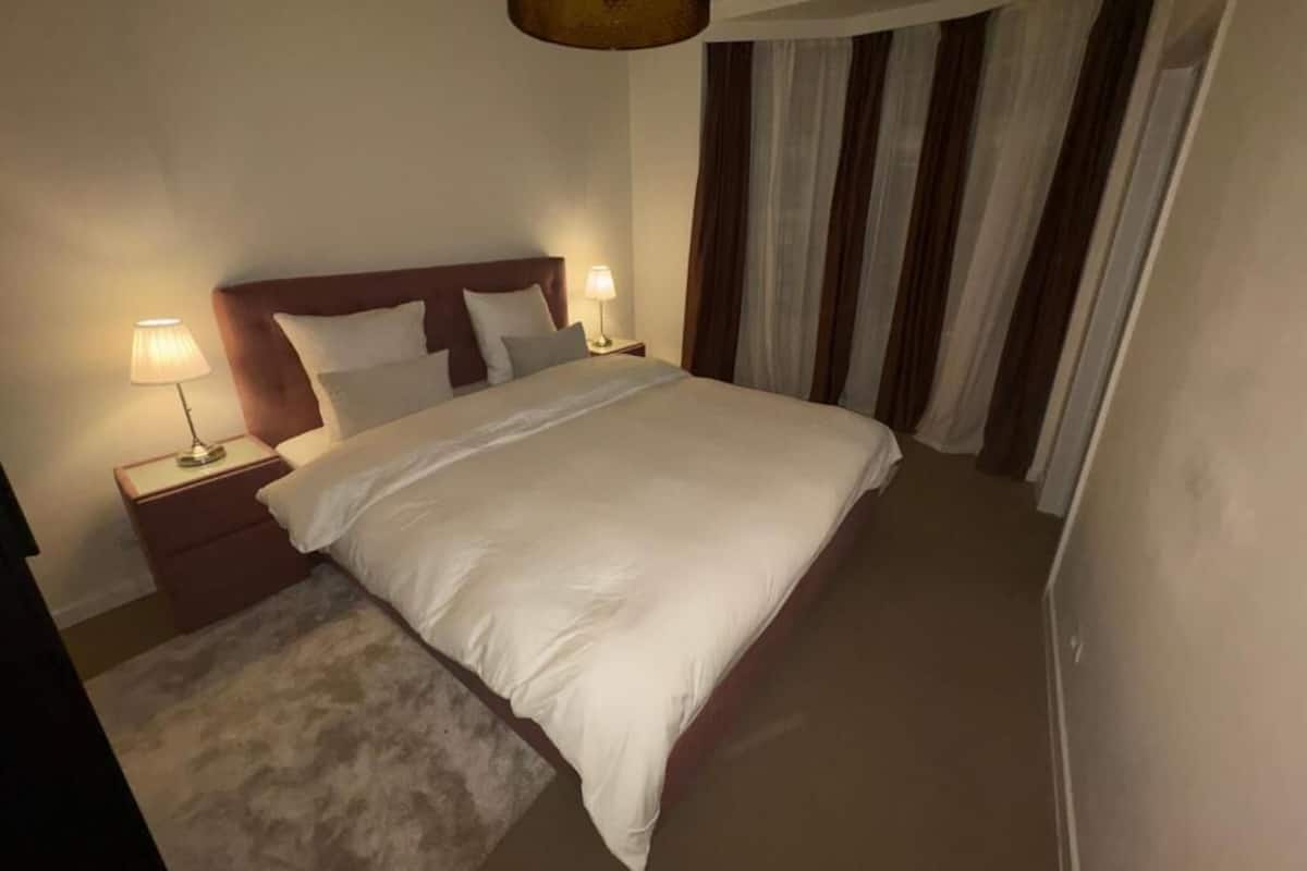 A neatly made bed with white linens, a wooden headboard, and two bedside lamps.