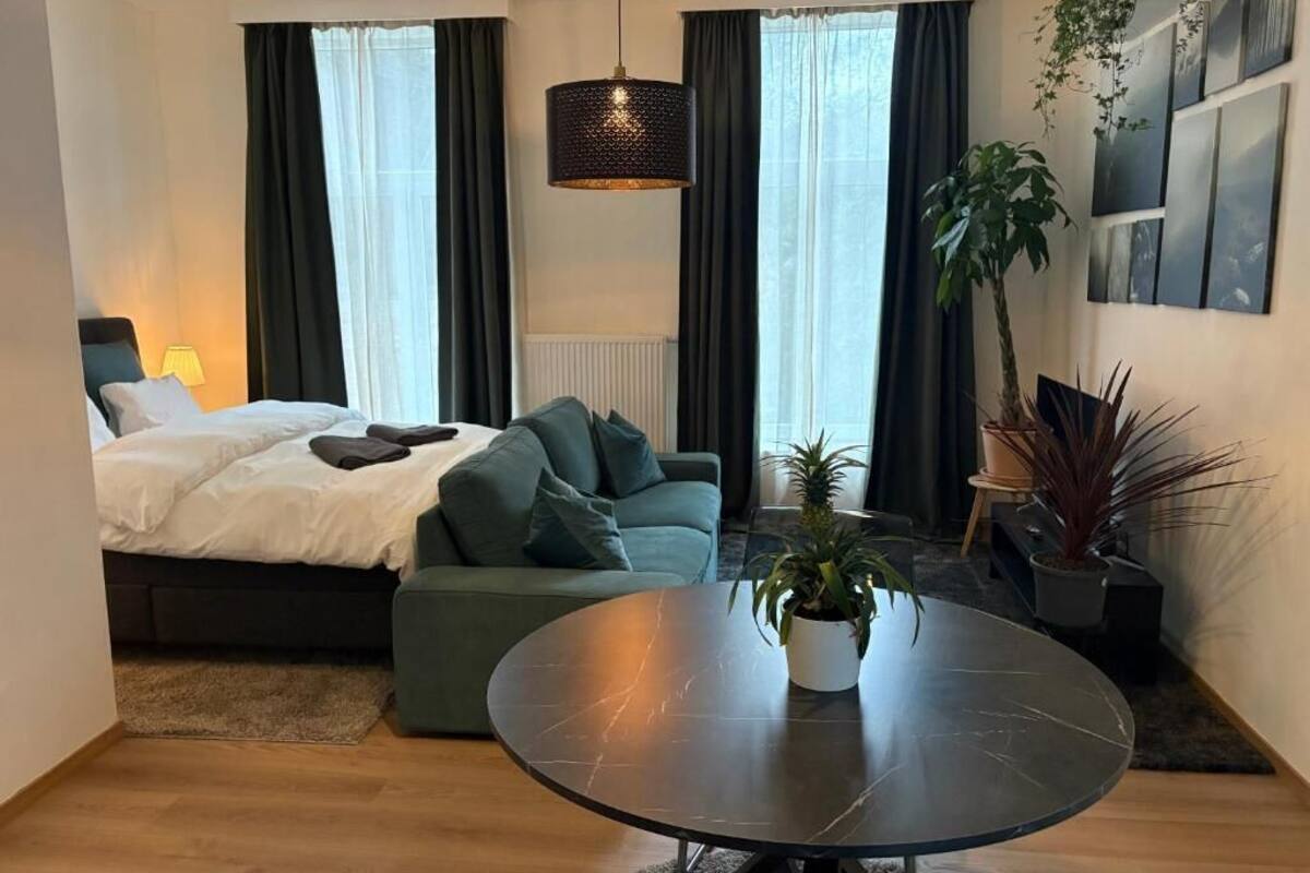 A modern hotel room with a bed, a sofa, a round table, and a large window with curtains.