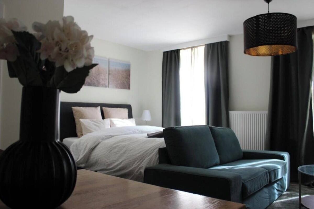 A hotel room with a bed, a green sofa, a vase with flowers, and a hanging light fixture.