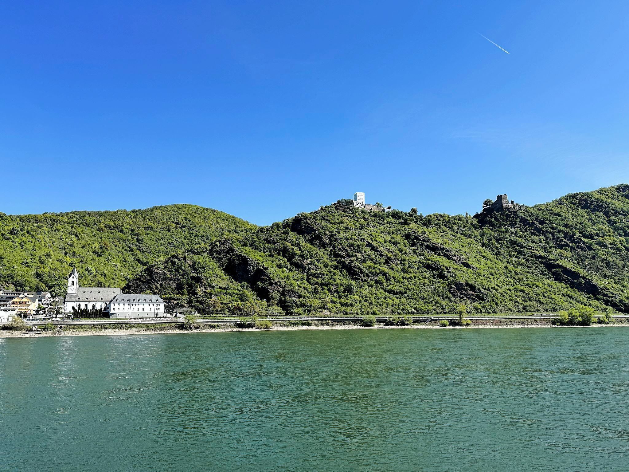 A hill with a building and a tower, a river, and a clear sky.