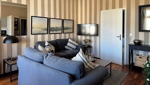 Olohuone, jossa on raidallinen tapetti, sohva, televisio, lamppu ja maljakko, jossa on kukkia.