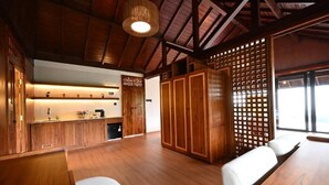 A wooden interior with a kitchen area, seating, and a view through a window. - Meadow Hills Villa by Mahaprana (Sukasada)