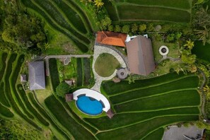 Una vista aerea di una proprietà con campi a terrazza, una piscina e un giardino circolare.