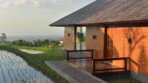 A modern house with a brick exterior, large glass windows, and a wooden deck. - Meadow Hills Villa by Mahaprana (Sukasada)