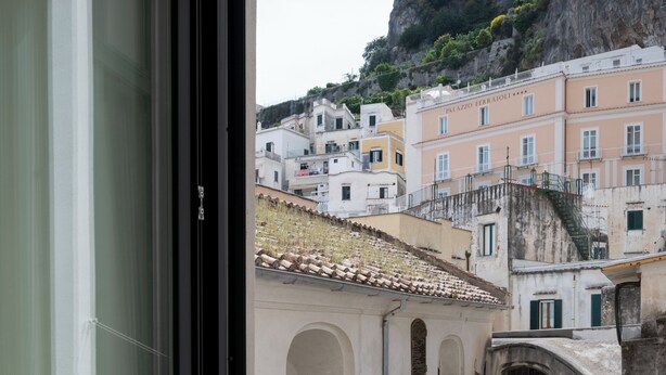 Un balcone con ringhiera in ferro battuto, vista su edifici con tetti in tegole di terracotta e un muro in pietra.