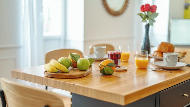Una mesa de desayuno con frutas, un florero y un croissant.