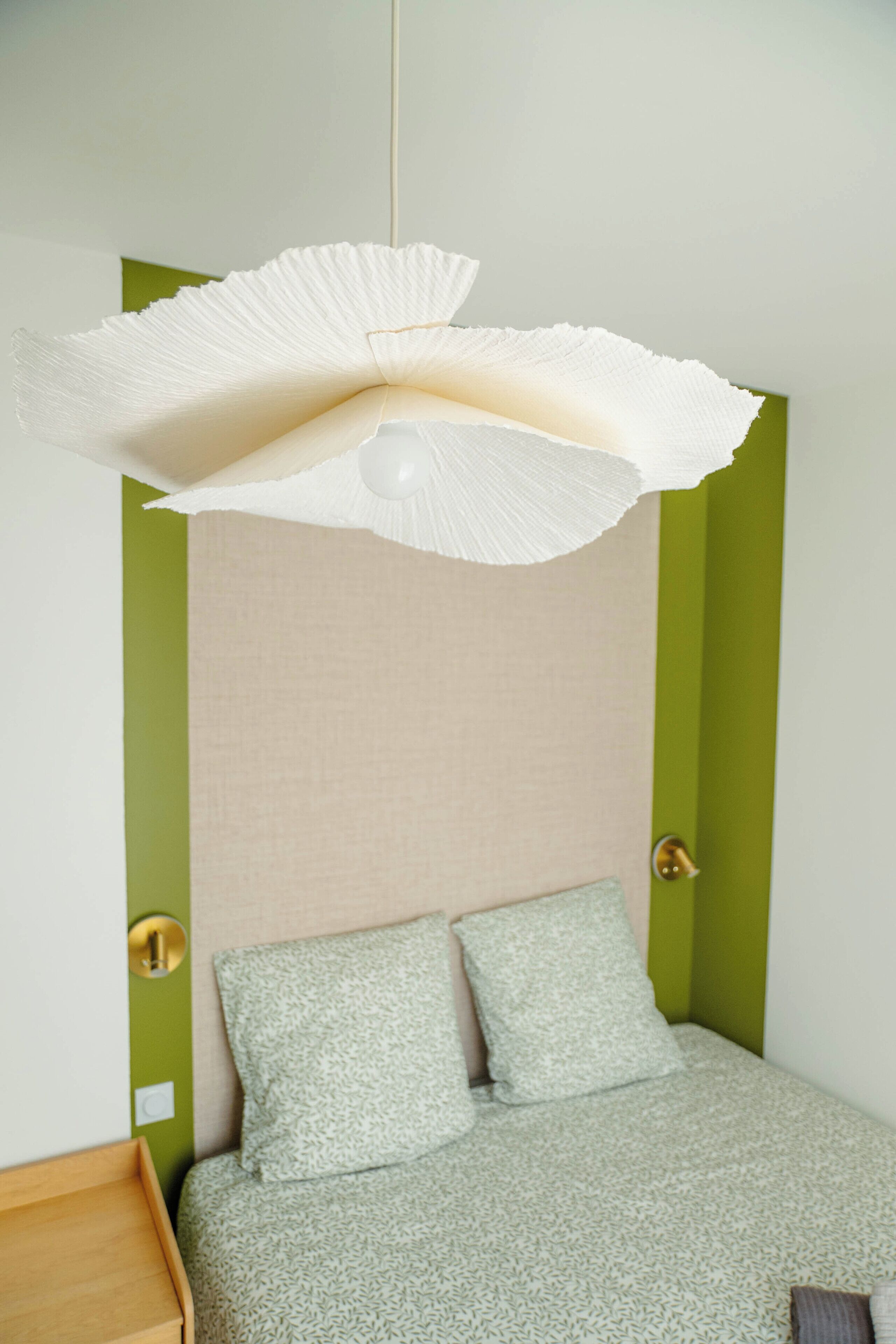 Ein Schlafzimmer mit Bett, Kissen, einer Hängeleuchte und einer grünen Wand.