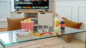 Una mesa de vidrio con un recipiente de palomitas, dos vasos, una botella de refresco y un paquete de aperitivos.