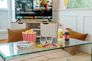 Ein Glastisch mit einer Popcornschale, zwei Gläsern, einer Limoflasche und einer Snacks-Packung.