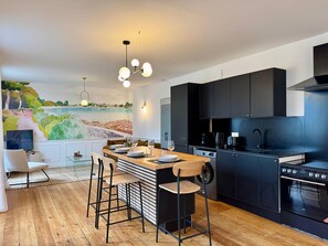 Eine moderne Küche mit einem Holzespeisetisch, schwarzen Schränken und einer großen Wandmalerei mit einer Küstenlandschaft.