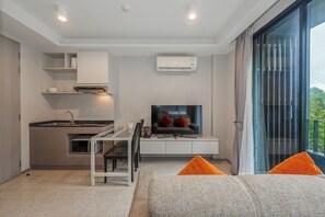A modern kitchen with a dining area, a flat-screen TV, and a large window with curtains. - Step 2 Surin Beach 1BR Rooftop, Gym & Pool C208 (Tambon Choeng Thale)