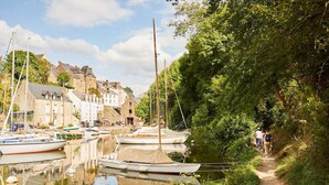 Ein Kanal mit vor Anker liegenden Booten, ein Weg entlang des Wassers und Gebäude im Hintergrund.