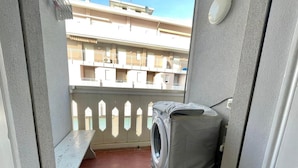Un balcón con lavadora, una banca y vistas a un edificio con balcones.
