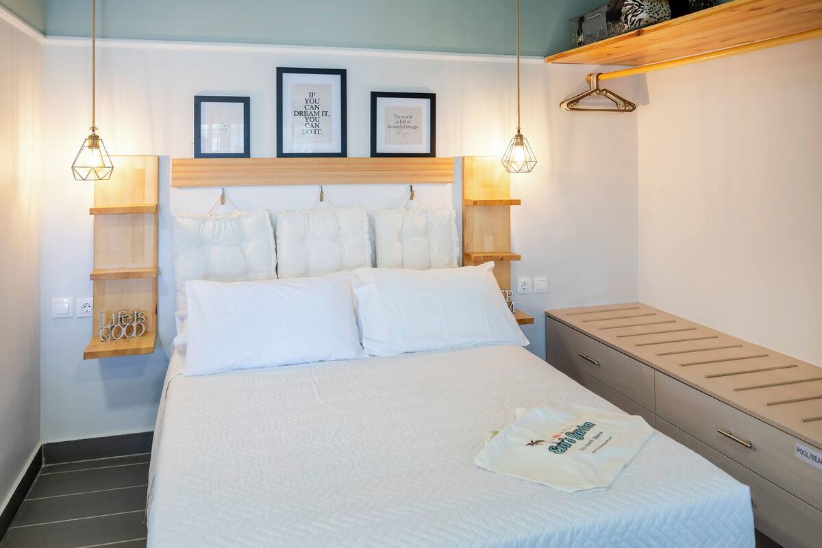 Una cama bien hecha con ropa blanca, un cabecero de madera y dos lámparas fijadas a la pared.