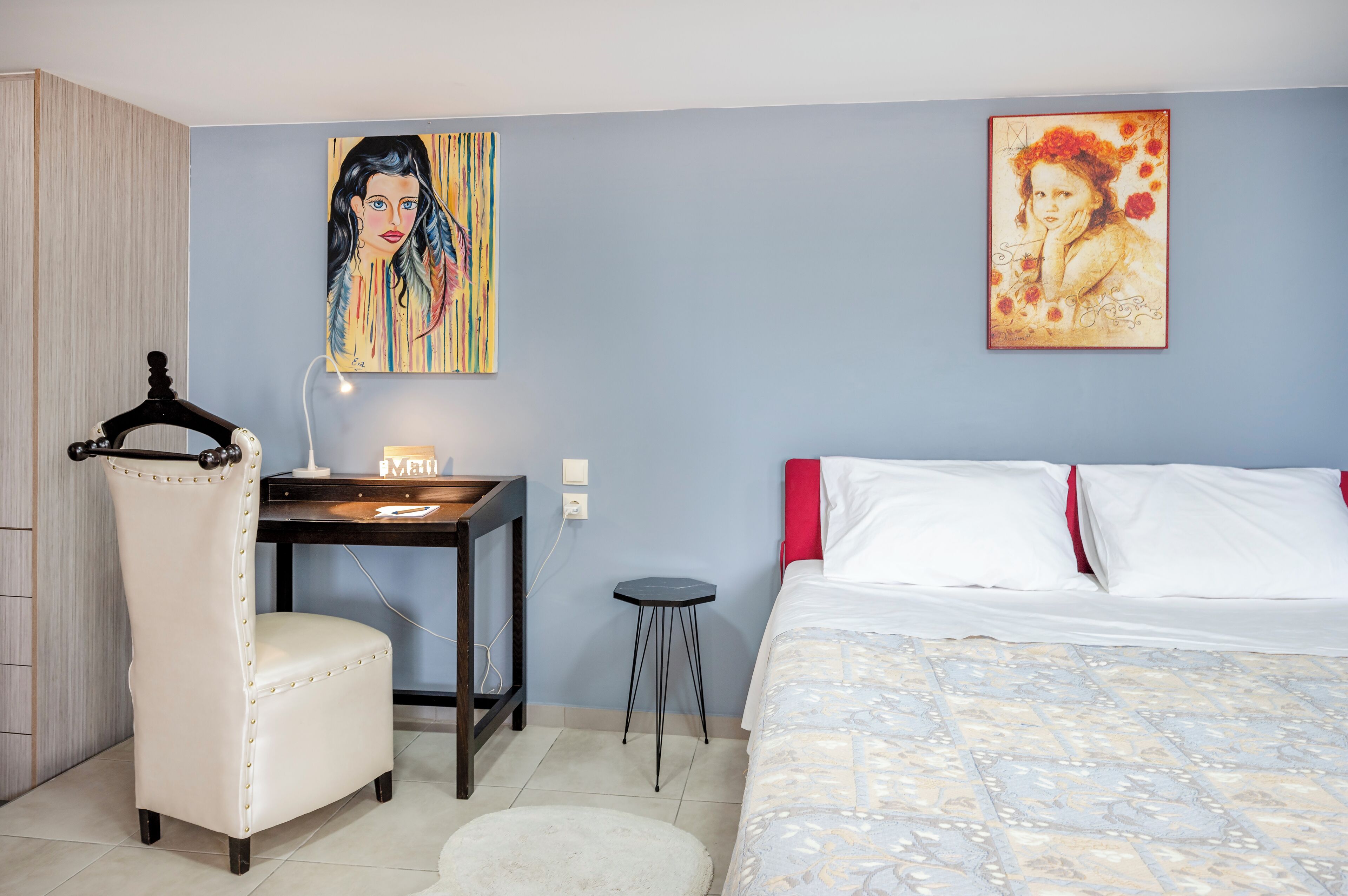 Una camera da letto con un letto, una scrivania, una sedia e due quadri appesi al muro.