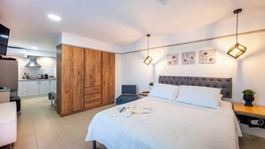 A bedroom with a bed, wooden wardrobe, bedside tables, and a view into the kitchen. - Homes Eva's Garden (Kos)