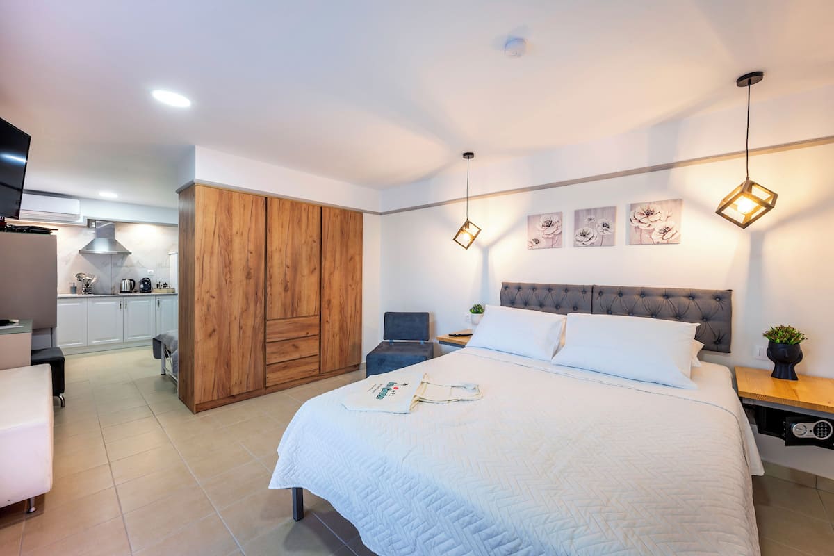 Un dormitorio con cama, armario de madera, mesitas de noche y vistas a la cocina.
