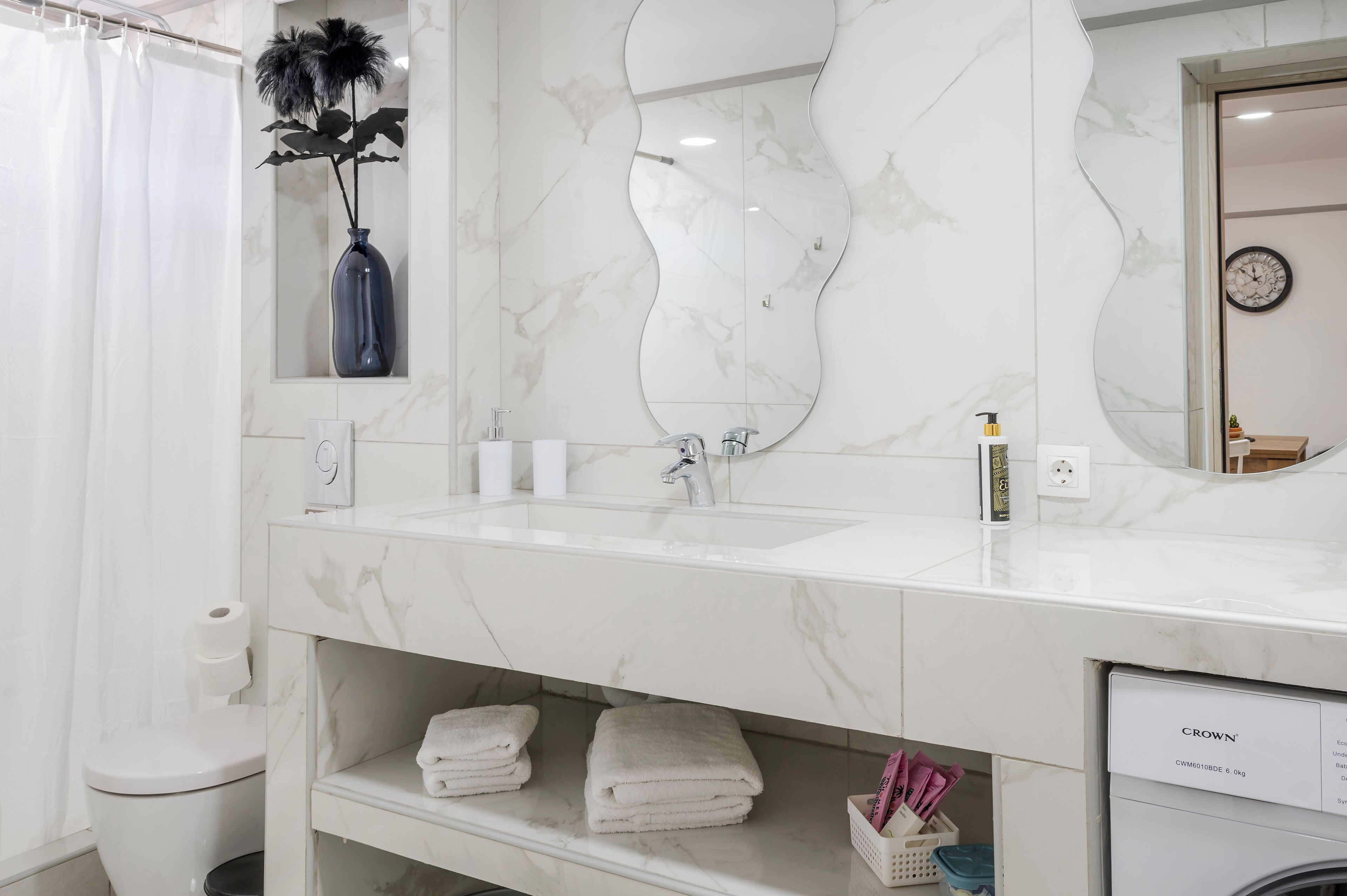 Een badkamer met een wit marmeren wastafel, een grote spiegel, een toilet en een douchegordijn.