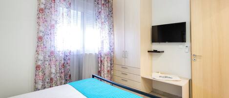 A bedroom with a bed, a TV mounted on the wall, a wardrobe, and a desk.