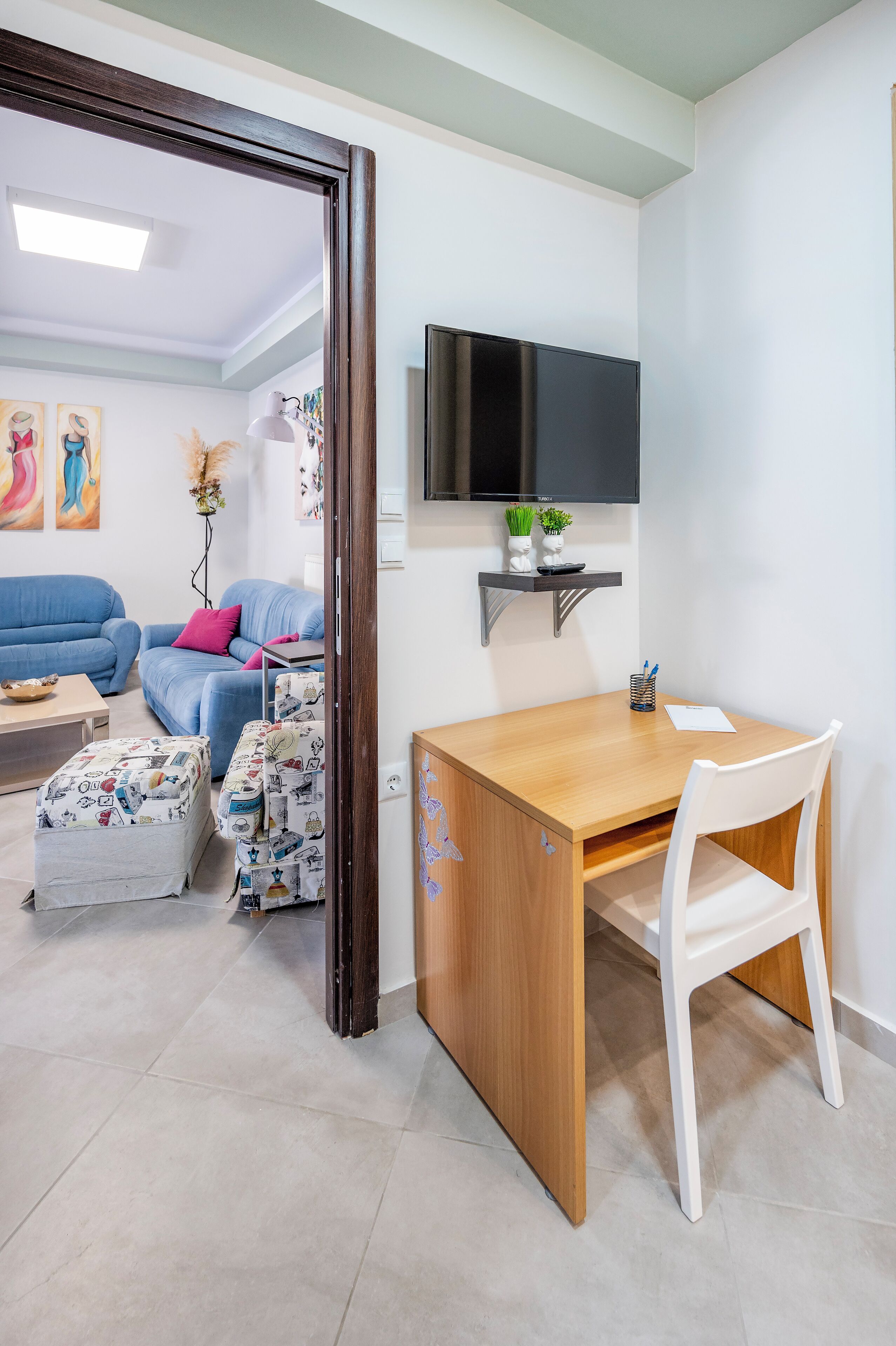 A room with a wooden desk, white chair, blue sofa, and a TV mounted on the wall.