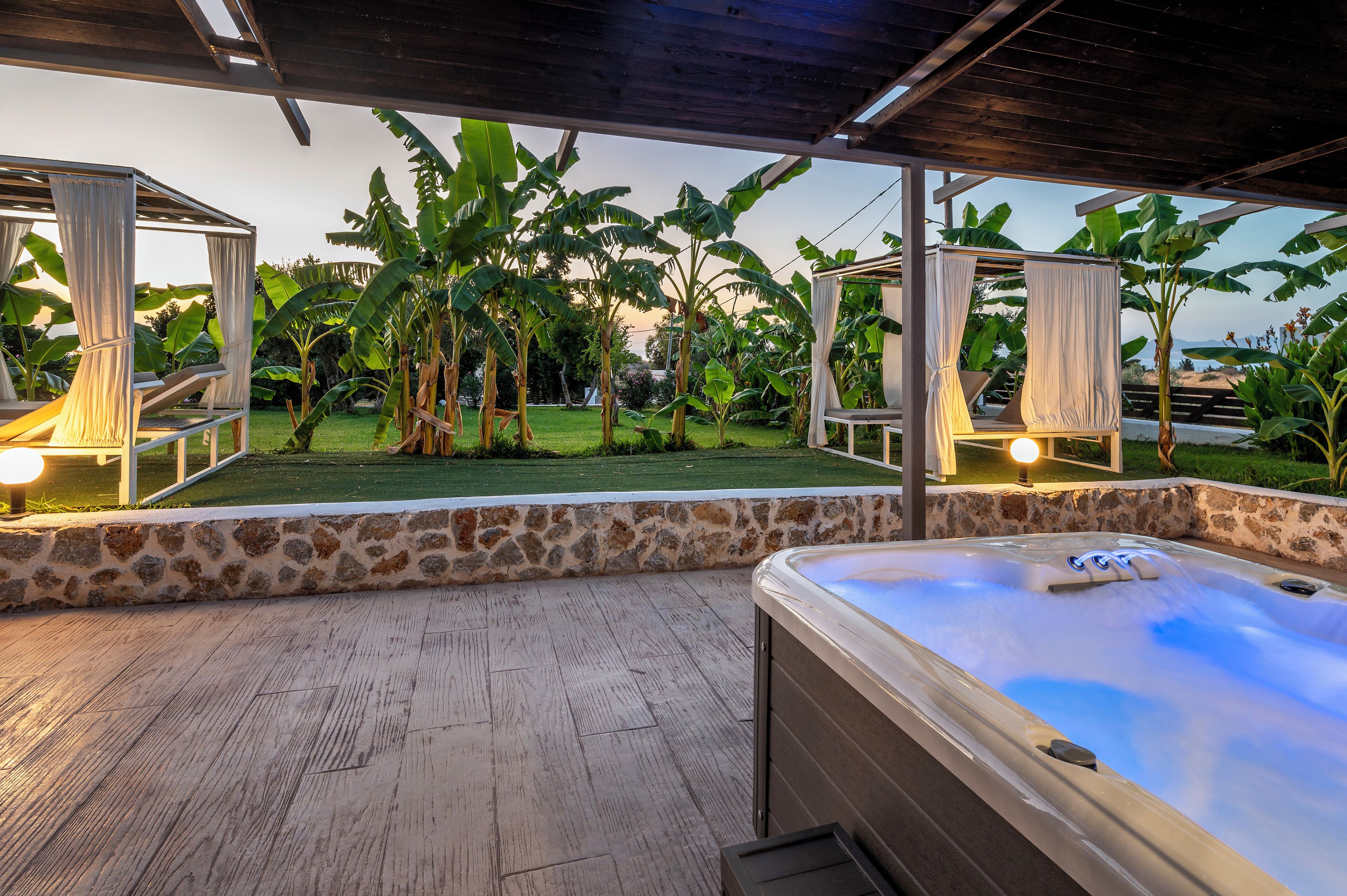 A hot tub with a stone wall and a grassy area with banana trees.