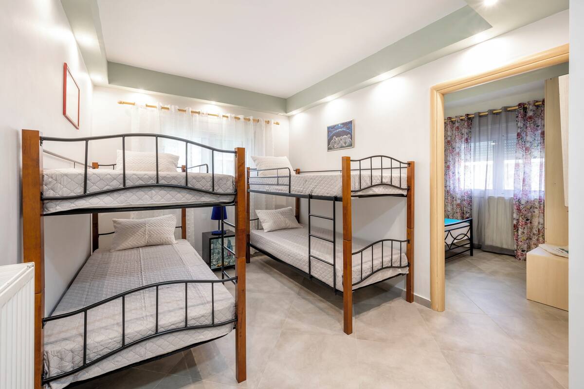 Habitación tipo dormitorio con literas, una mesita, una silla y una ventana con cortinas.