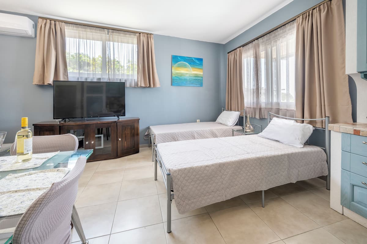 Habitación de hotel con dos camas, televisión, mesa de comedor y un cuadro en la pared.