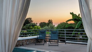 A poolside area with a view of the sunset, two lounge chairs, and a stone wall. - Homes Eva's Garden (Kos)