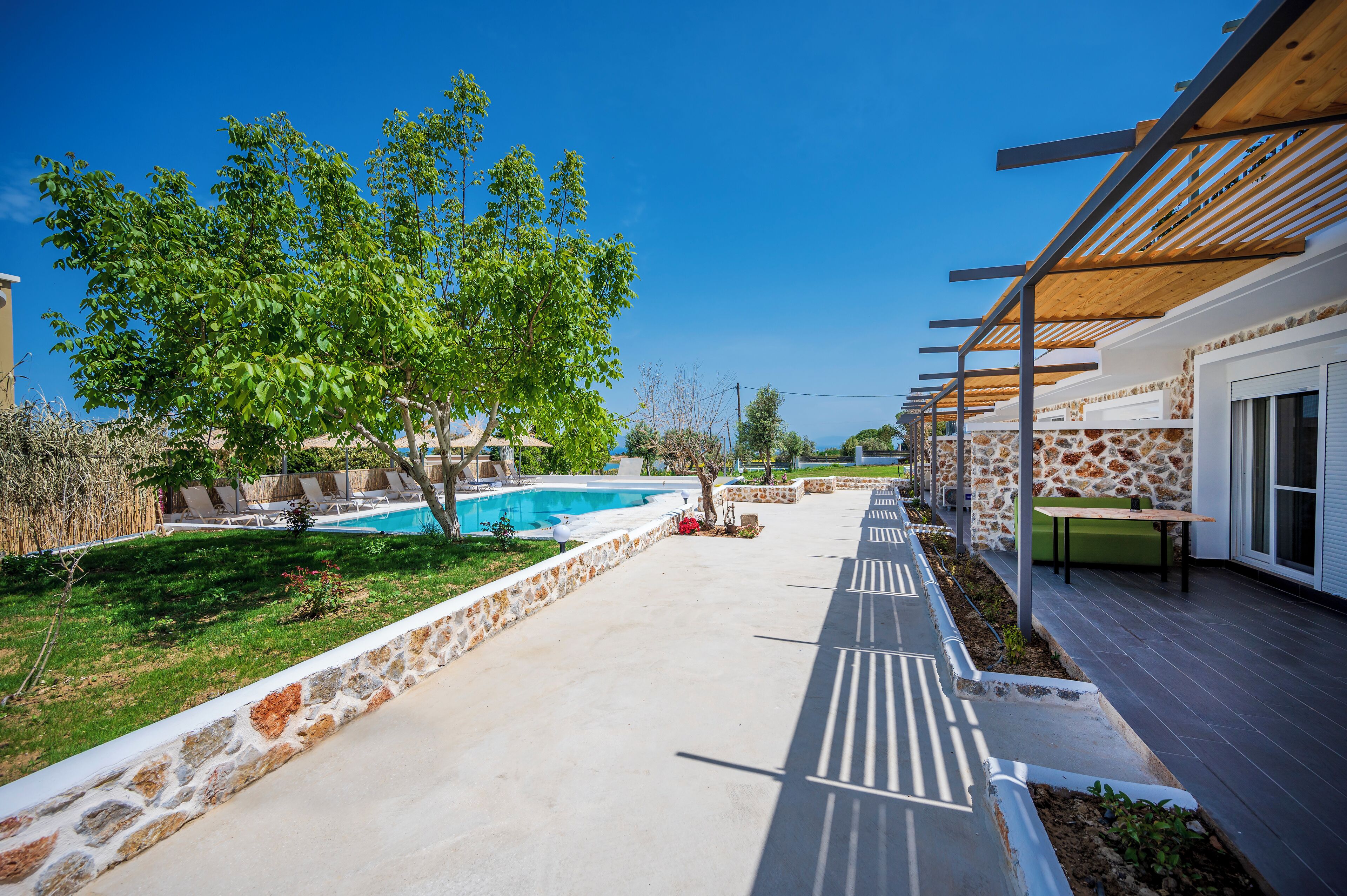 Ein Poolbereich mit Steinmauer, einer Pergola und Blick auf ein Gebäude mit einer Steinfassade.