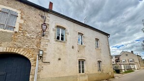 Un bâtiment en pierre de deux étages, avec une porte bleu foncé, de nombreuses fenêtres et une vue sur la rue.