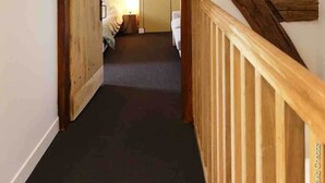 Un escalier avec des poutres en bois apparentes et une rampe en bois, menant à une pièce comprenant un lit et une table de chevet.