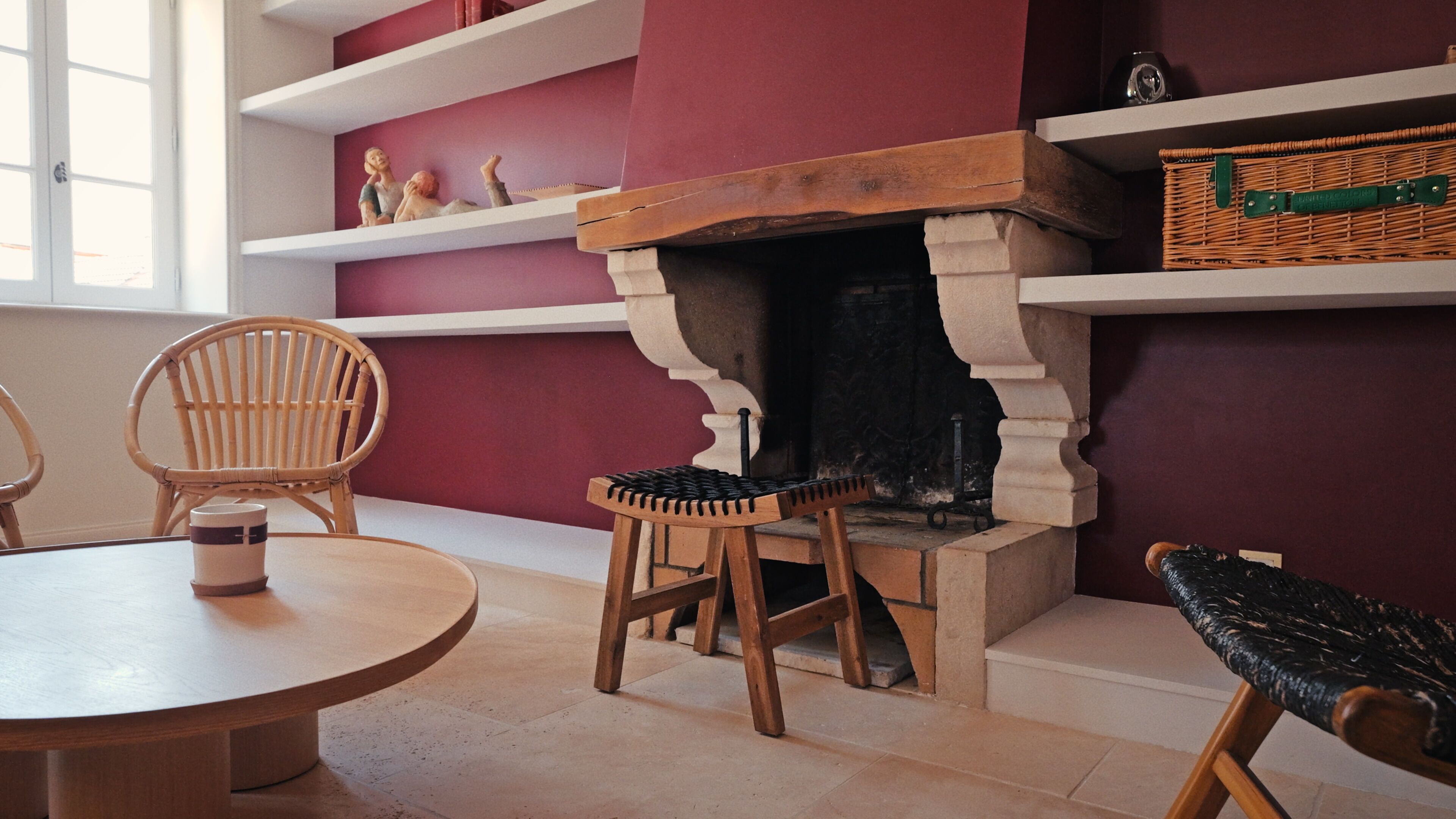 Una habitación con chimenea, sillas de madera, una mesa redonda y estanterías con objetos decorativos.