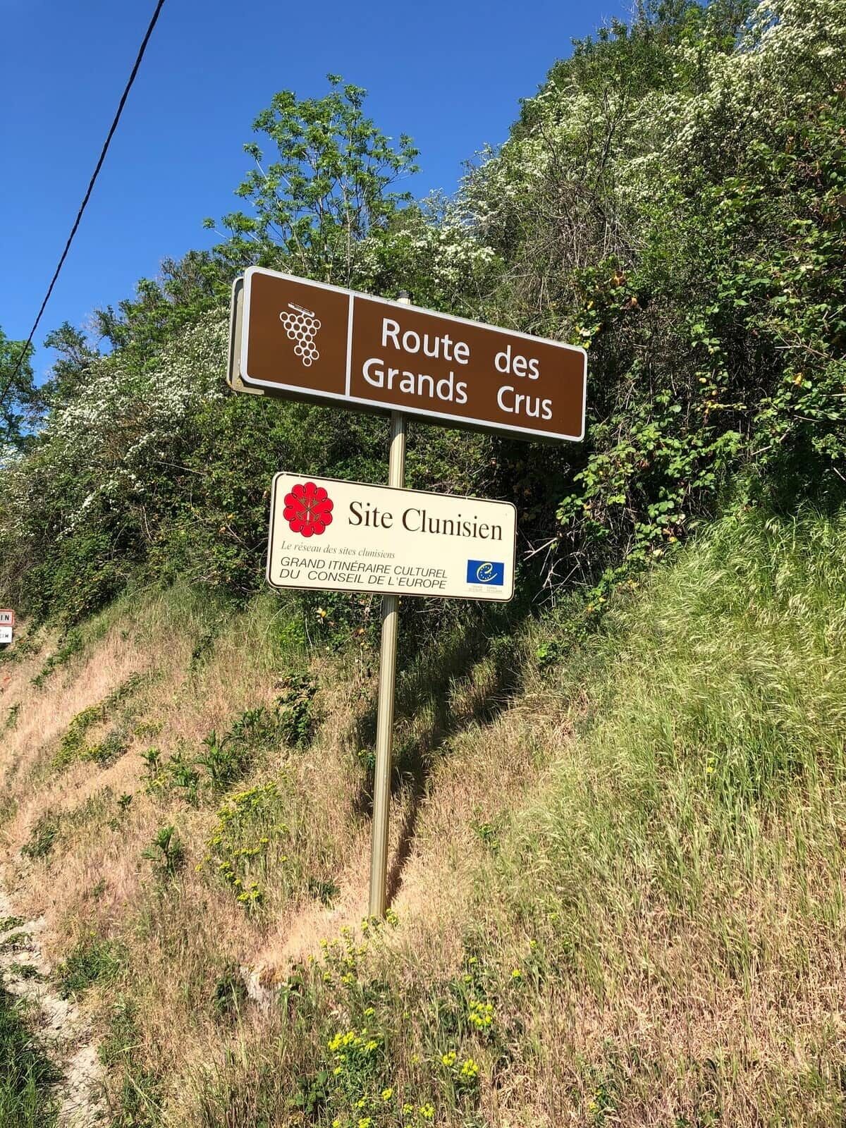 A signpost with 'Route des Grands' and 'Site Clunisien' text, indicating a route and a cultural site.