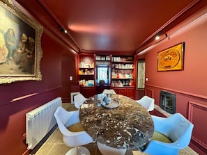 Ein Esszimmer mit einem Marmortisch, weißen Stühlen, einem Bücherregal und einem gerahmten Gemälde.