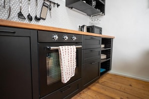 Una cocina con encimera de madera, horno empotrado, un perchero con utensilios y salpicadero azulejado.