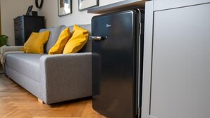 Un petit réfrigérateur, un canapé gris avec des coussins jaunes et un plancher en bois.