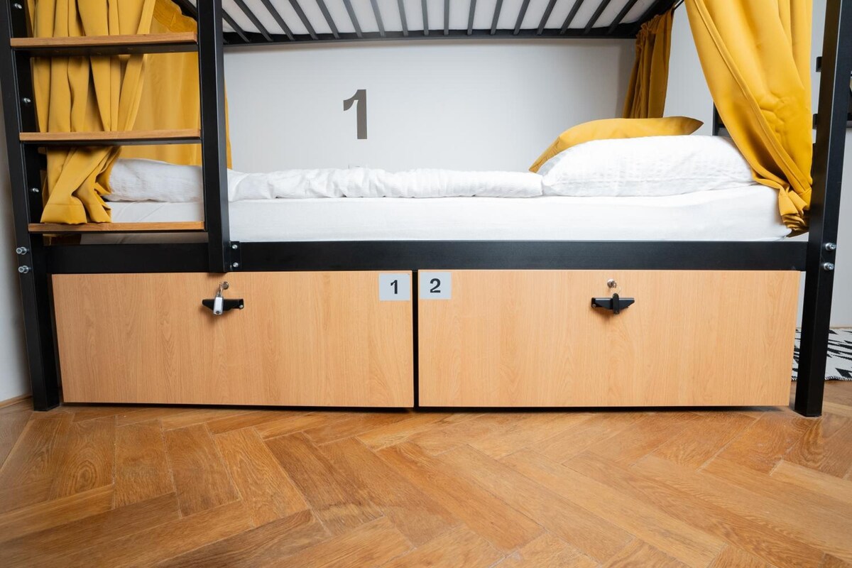 Een stapelbed met een bord met het cijfer 1, houten opbergvakken en gele gordijnen.