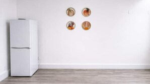 A room with a white refrigerator, wooden flooring, and four wall-mounted decorative plates. - Elegant Flat | 2-Min Walk to Watford Junction (Watford)