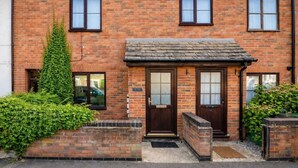 A two-story brick house with a front door, two windows on the ground floor, and a small porch area. - Elegant Flat | 2-Min Walk to Watford Junction (Watford)