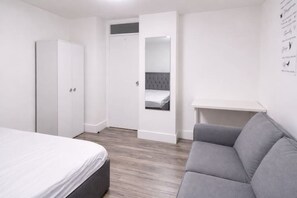 Ein Schlafzimmer mit einem Bett, einem grauen Sofa, einem Kleiderschrank und einem kleinen Schreibtisch mit Spiegel.